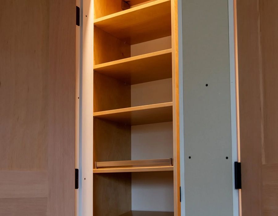 Open wooden cabinet with four shelves, lit from above; light-colored wood.
