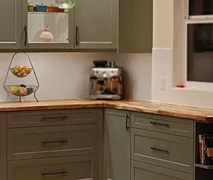 Green kitchen cabinets with wooden countertops and a silver toaster.