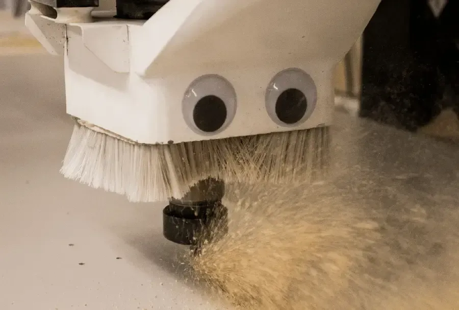 A CNC machine with googly eyes cutting wood, creating sawdust.