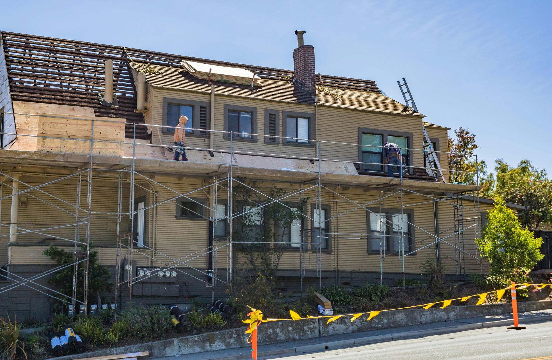 Scaffolding around a two-story house under renovation, with workers on the upper level.