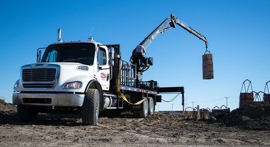 A white truck with a crane attached to it is parked in a dirt field.