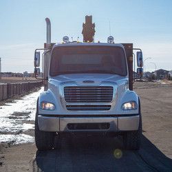 A white truck with a crane on top of it is parked in a parking lot.
