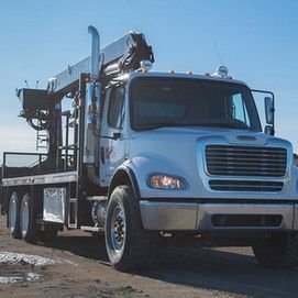 A large white truck with a crane on the back is parked on a dirt road.