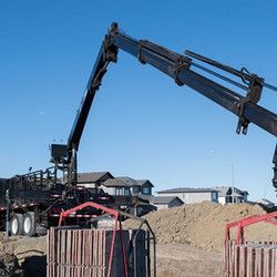 A truck with a crane attached to it is driving down a dirt road.