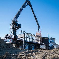 A truck with a crane attached to the back of it is sitting in a dirt field.