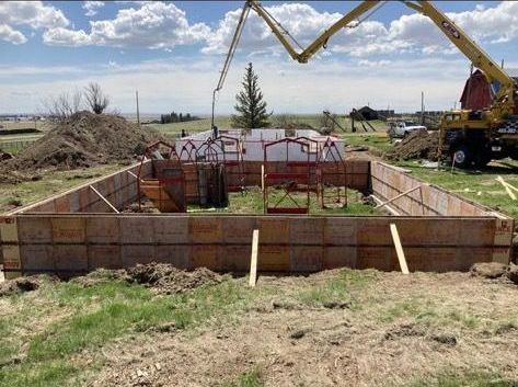 A crane is pouring concrete into a foundation in a field.