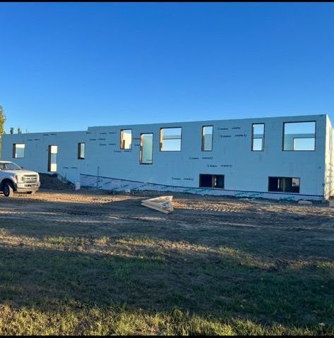 A white truck is parked in front of a large white building under construction.