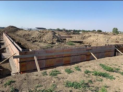 A large concrete wall is being built in a dirt field.