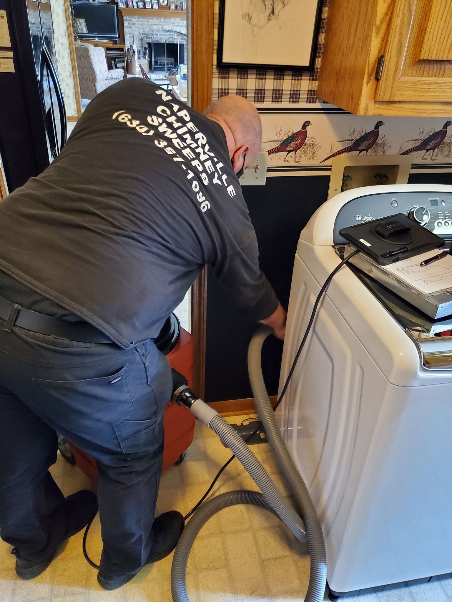 A man in a black shirt is using a vacuum cleaner to clean a washer and dryer.