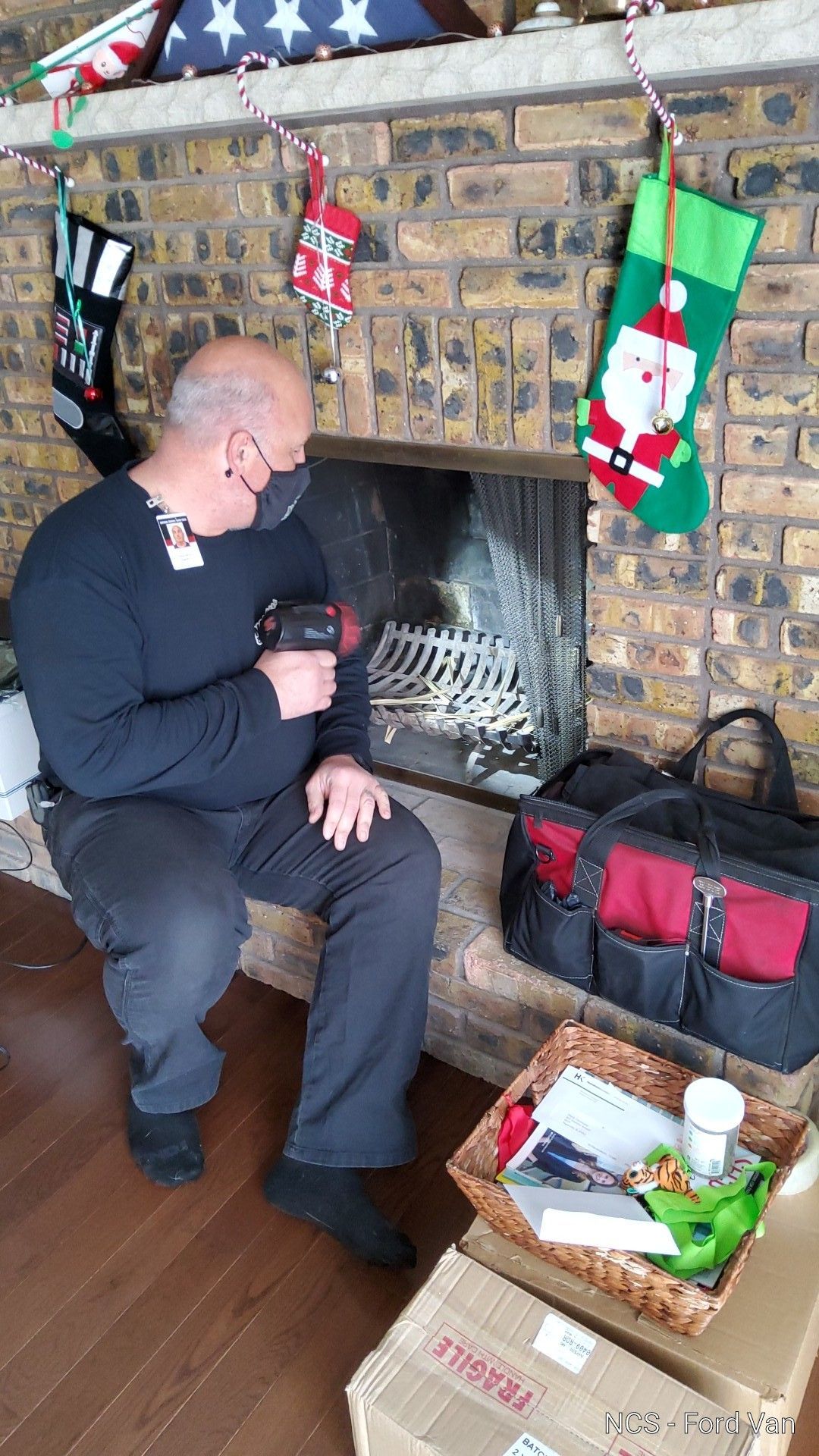 A man is sitting in front of a fireplace with a drill.