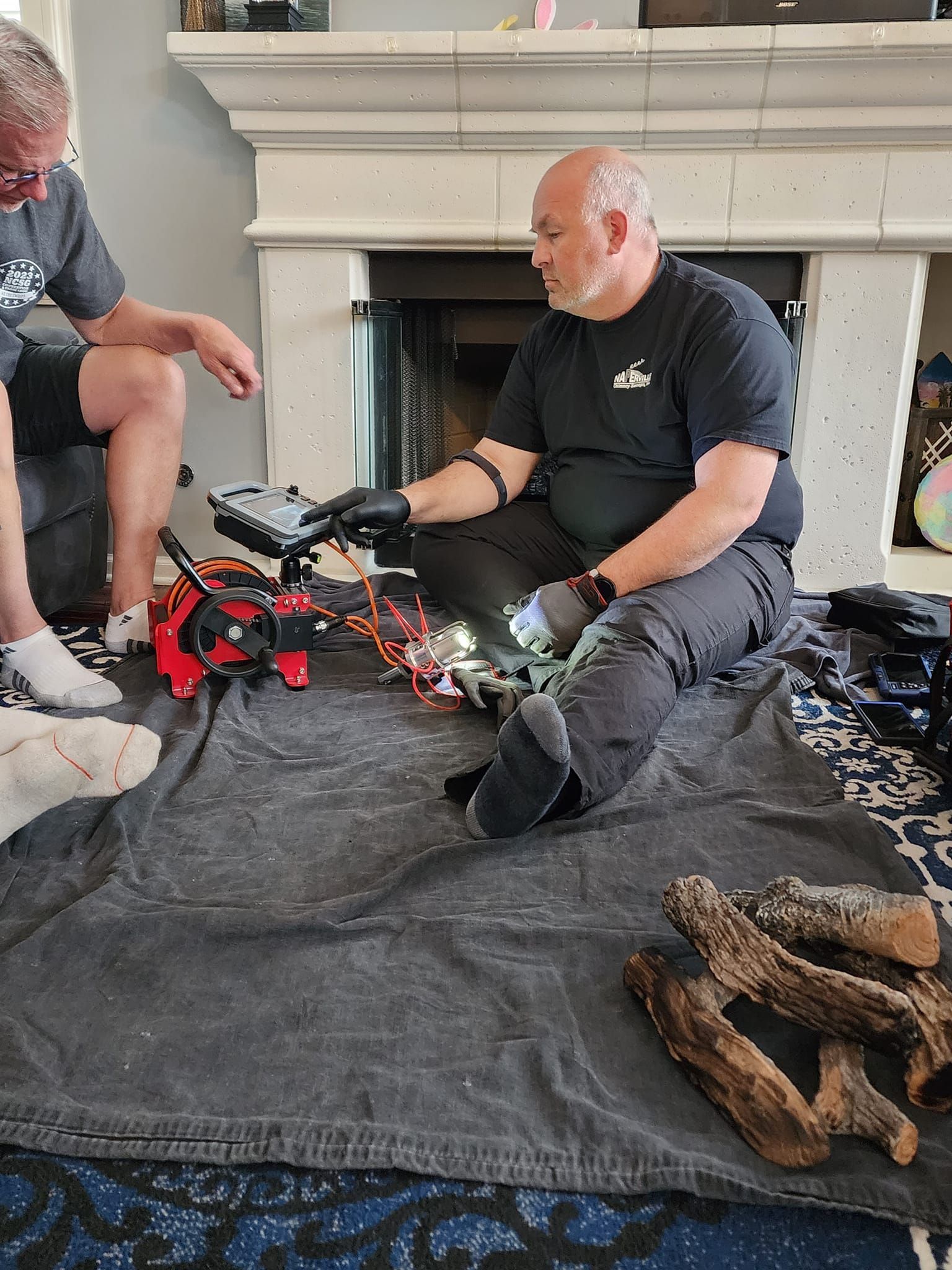 Two men are sitting on the floor in front of a fireplace.