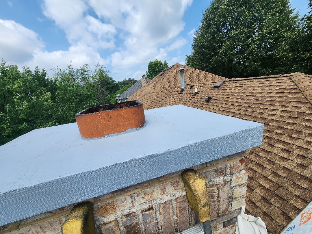 A chimney on top of a brick building with a roof in the background.