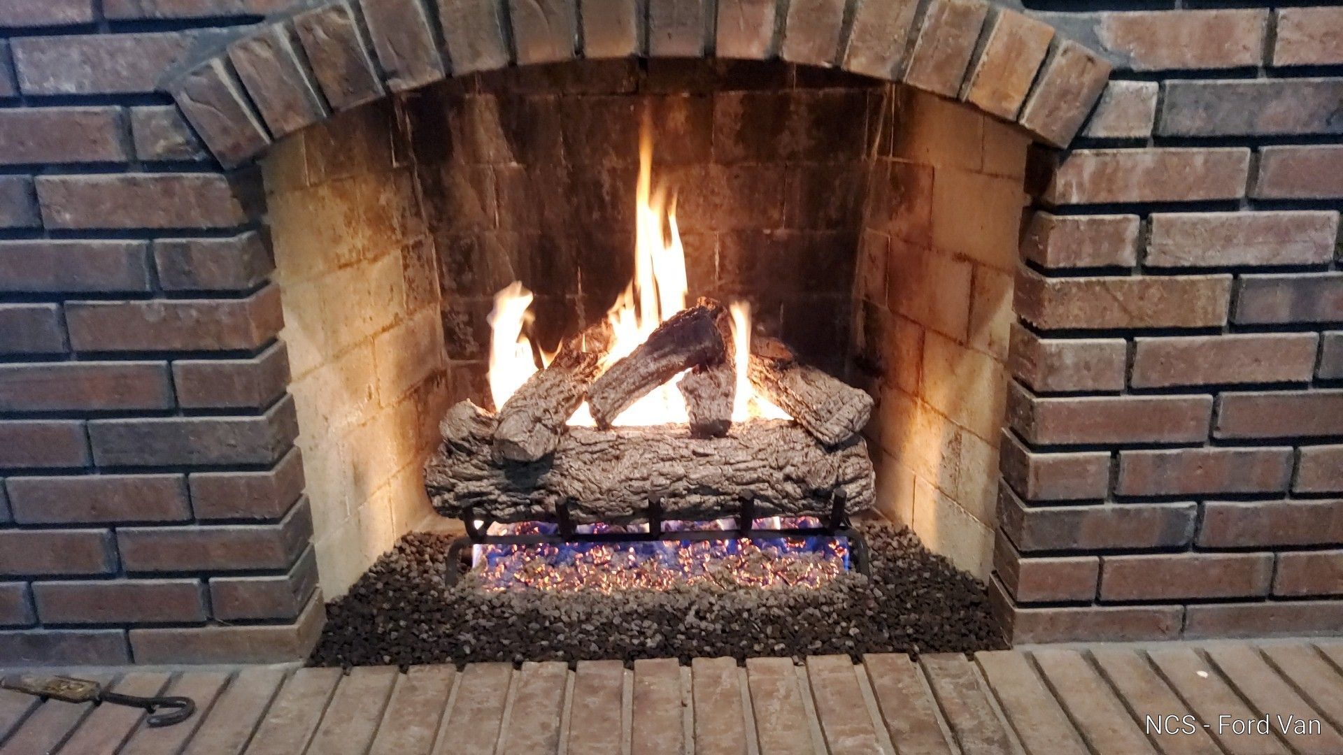 Fireplace with burning logs inside brick hearth, flames and embers visible.