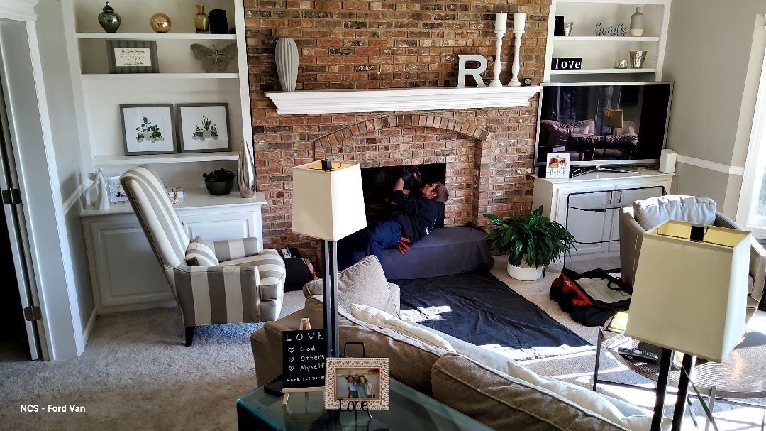 A man is sitting in front of a fireplace with a drill.