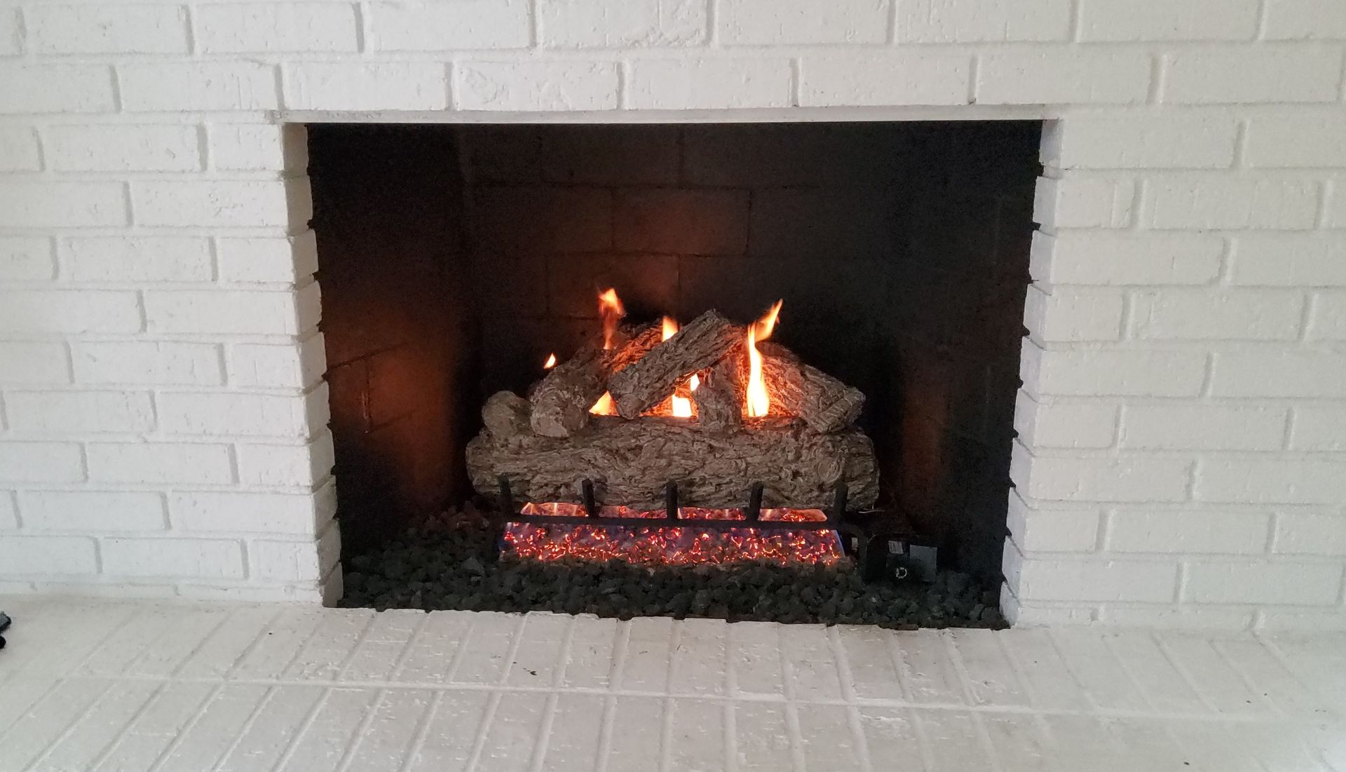 Fireplace with gas logs burning inside a brick surround.