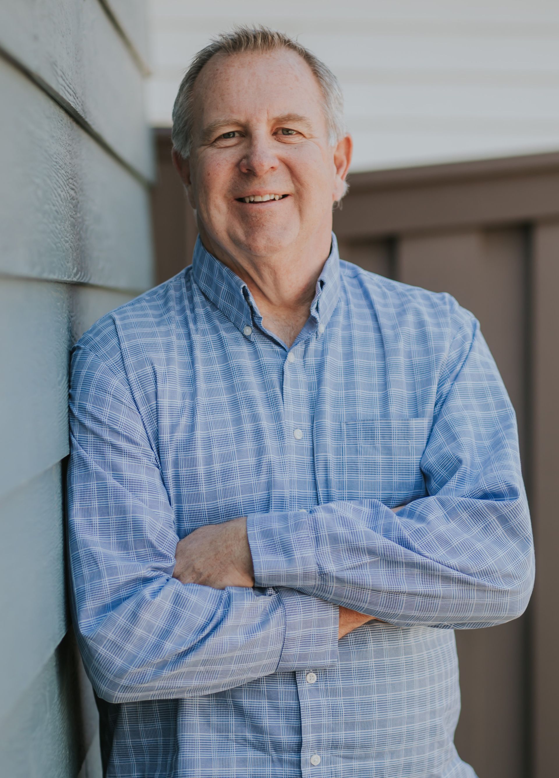 A man in a blue shirt is leaning against a wall with his arms crossed.