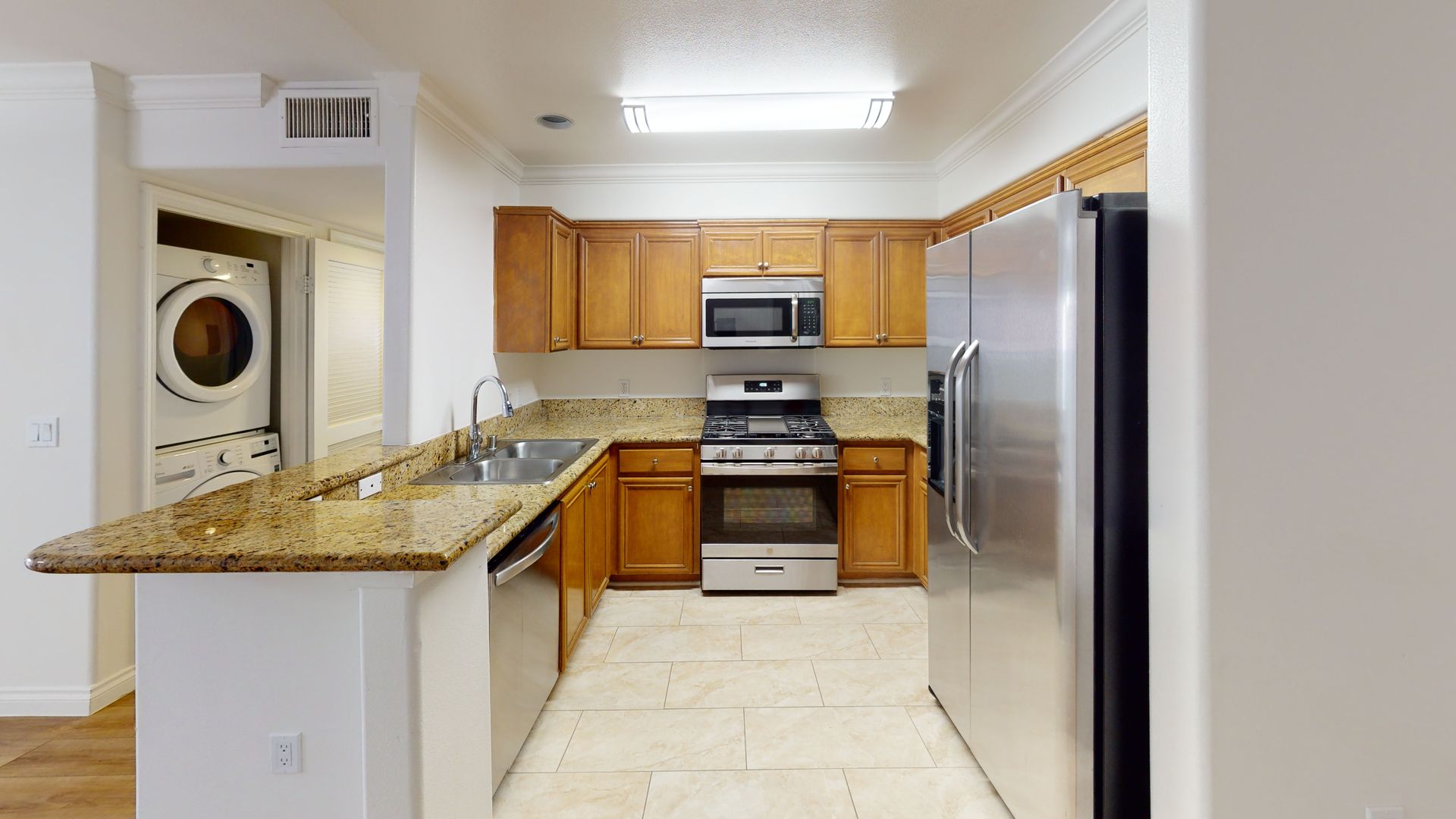 Kitchen with granite countertops, stainless steel appliances, and wooden cabinets. Washer and dryer in background.