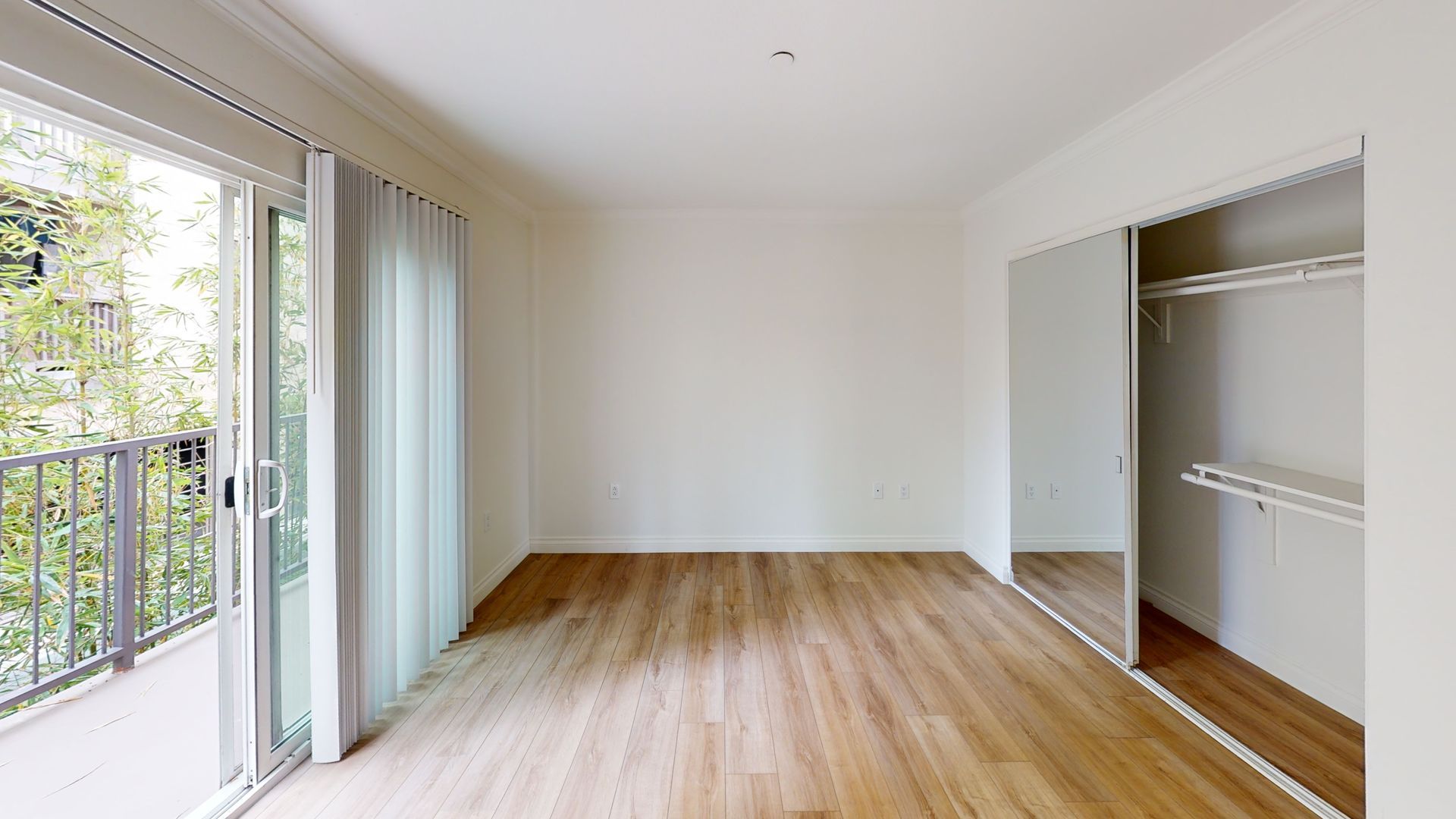 Empty room with wood floors, balcony doors, and mirrored closet.