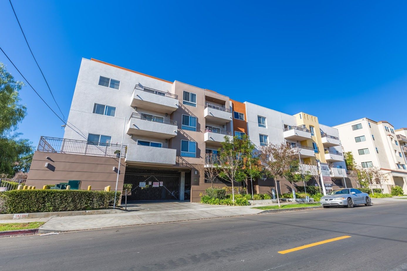 Multi-story apartment building with balconies, street view. Bright blue sky.