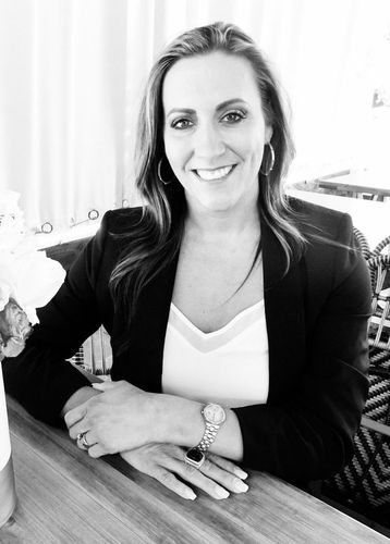 Brooke Pierce is sitting at a table with her hands folded and smiling in a black and white photo.