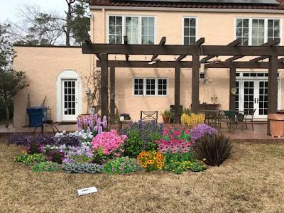 A colorful flower bed in front of a peach-colored house with a wooden pergola.