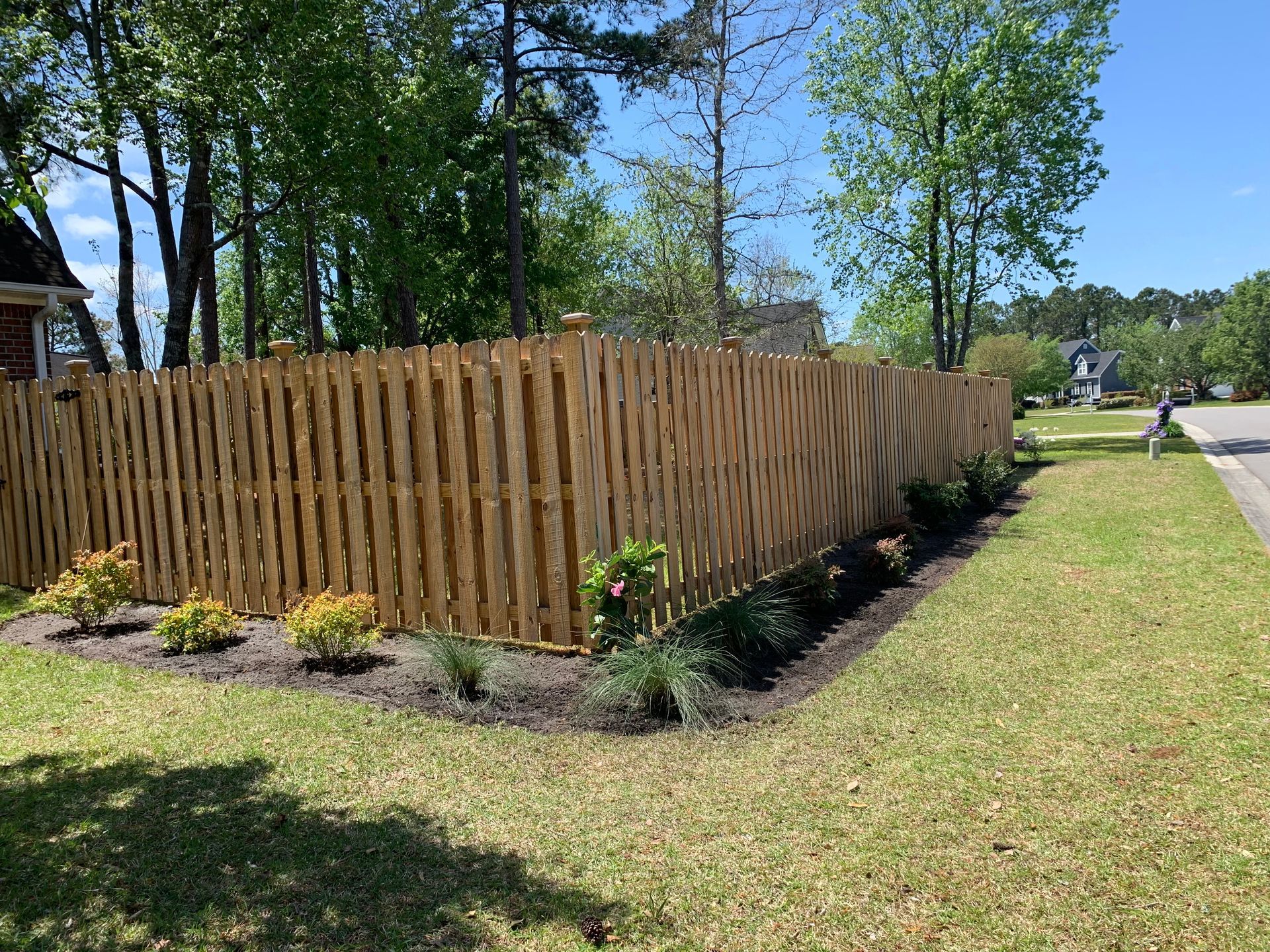 Wooden fence bordering a well-manicured lawn with landscaping.