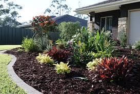 A colorful landscaped garden bed in front of a house, mulched with dark wood chips.