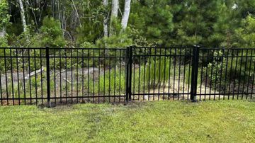 Black metal fence in a grassy yard, with trees in the background.