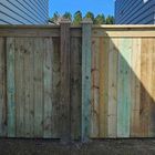 Wooden fence with two square posts, varying green and brown tones, under a blue sky.