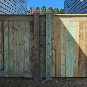 Wooden fence with two square posts, varying green and brown tones, under a blue sky.