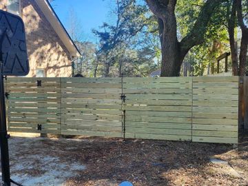 Horizontal wooden fence with three sections, under a tree, beside a house, on a sunny day.