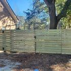 Wooden horizontal slat fence with gate, in front of a house, tree, and blue sky.
