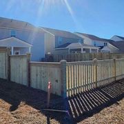 Wooden fence in a sunny backyard with several houses visible in the background.