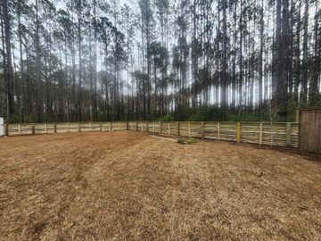 Wooden fence surrounding a gravel yard, with tall trees in the background under an overcast sky.