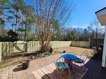 Backyard with brick patio, table and chairs, fenced yard, and bare tree under blue sky.