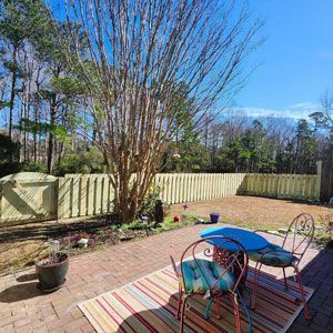Backyard patio with a table, chairs, and a fence on a sunny day.