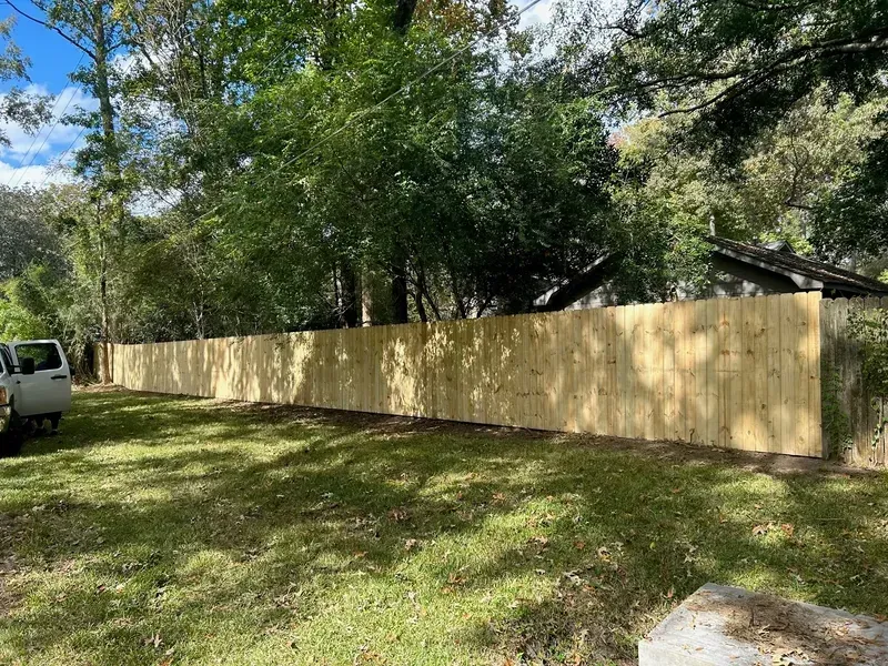 Long wooden fence in a grassy yard, trees in the background, partly cloudy sky.