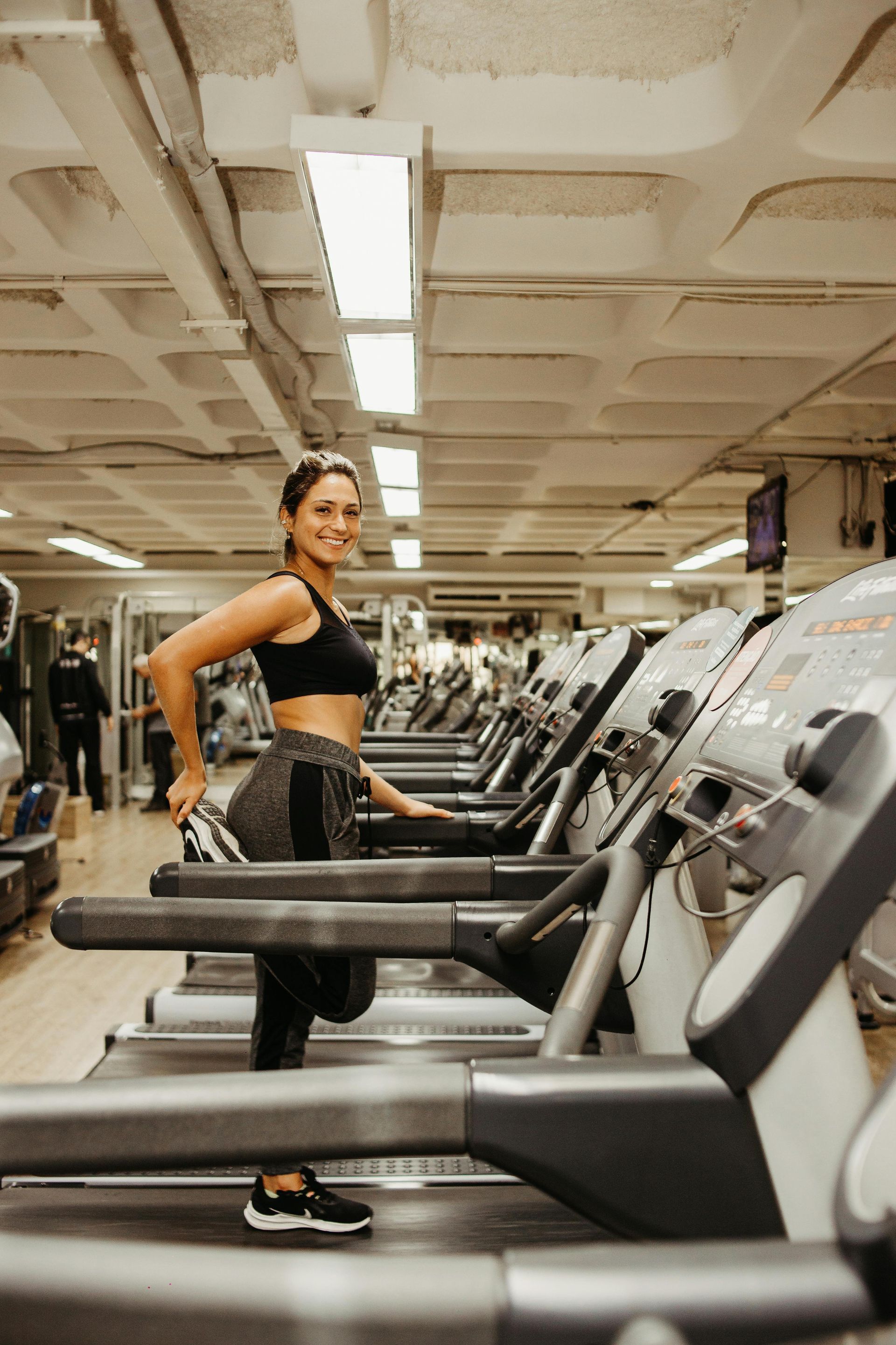 A woman is standing on a treadmill in a gym.