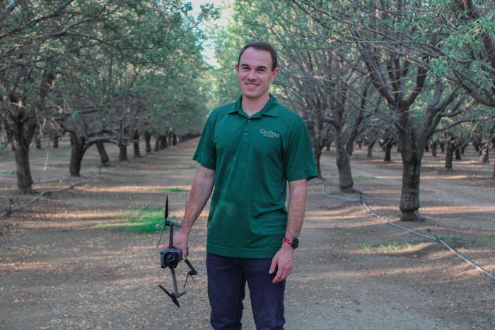 A man in a green shirt is holding a drone in a field.