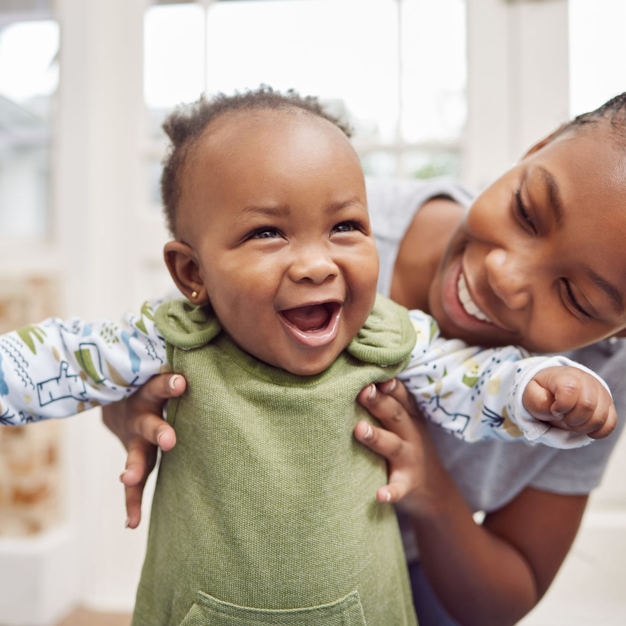 A mother is holding her young girl under the arms. The girl is smiling and wearing a green sweater. 