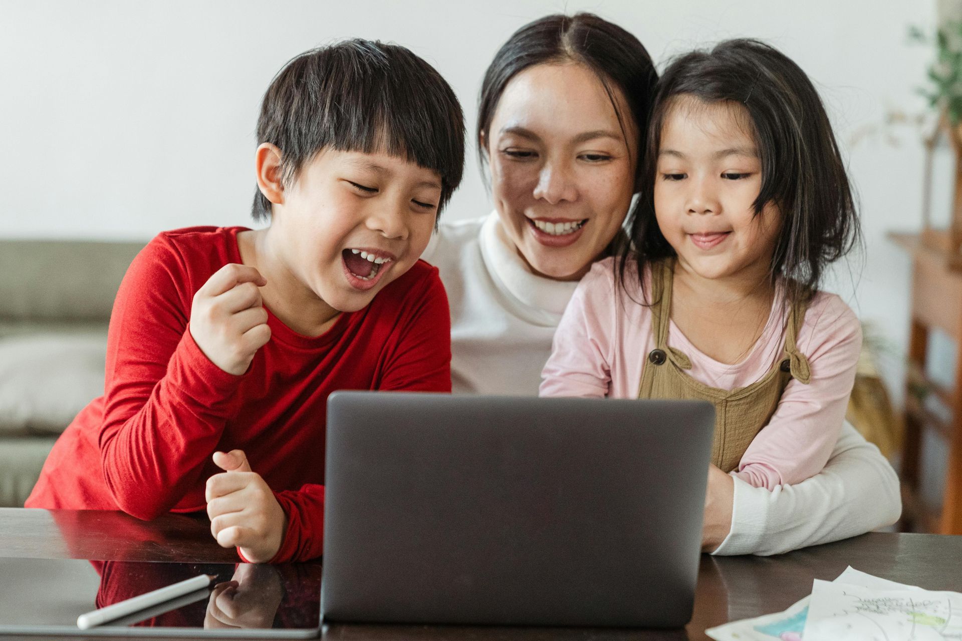 A mom with her young son and daughter are sitting in front of a laptop computer and smiling.