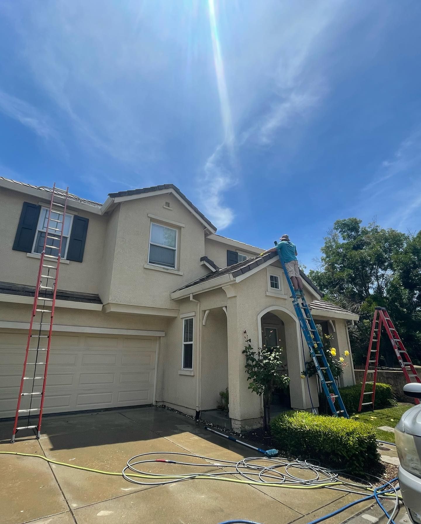 A man is standing on a ladder painting the roof of a house.