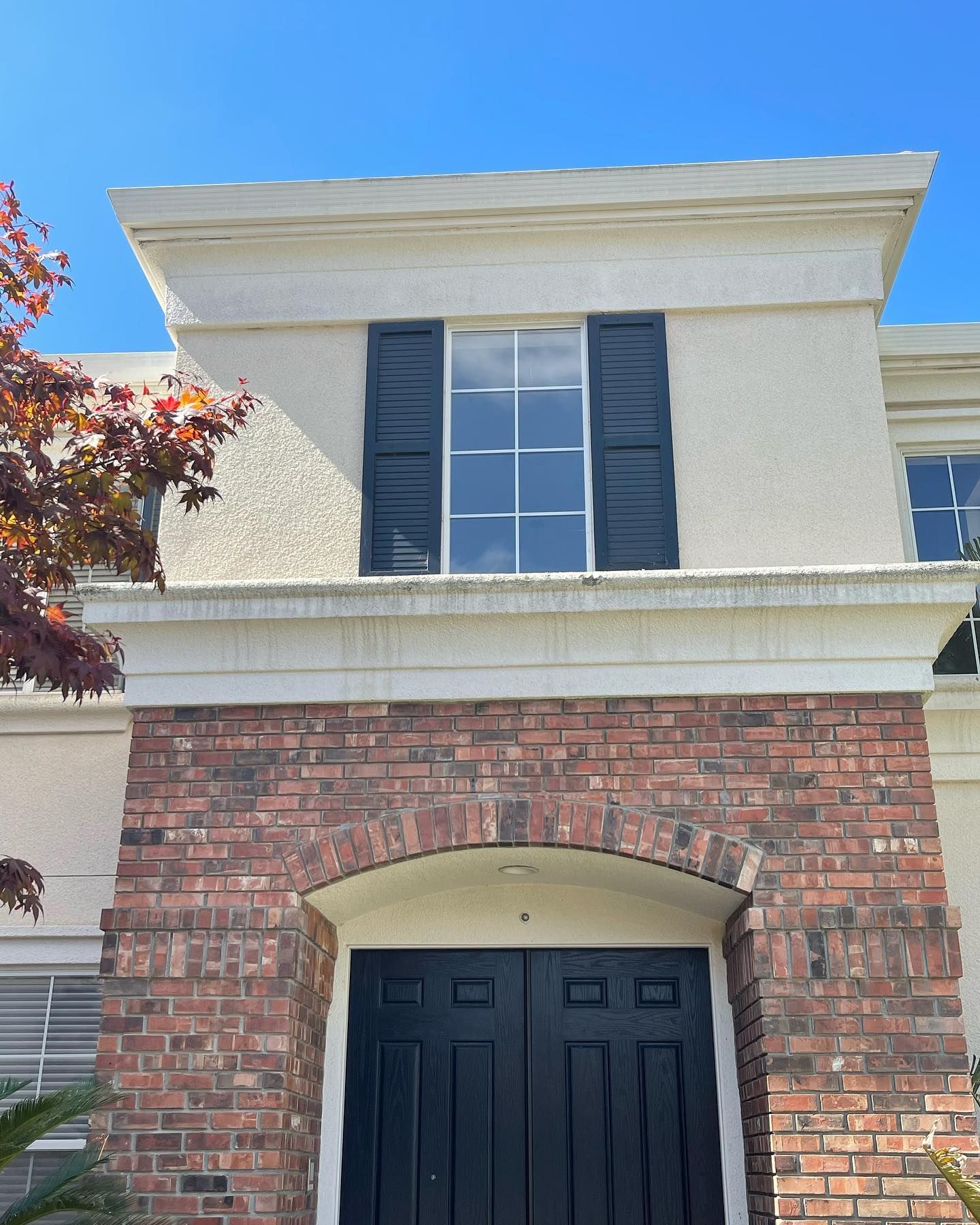 The front of a brick house with a black door and black shutters.