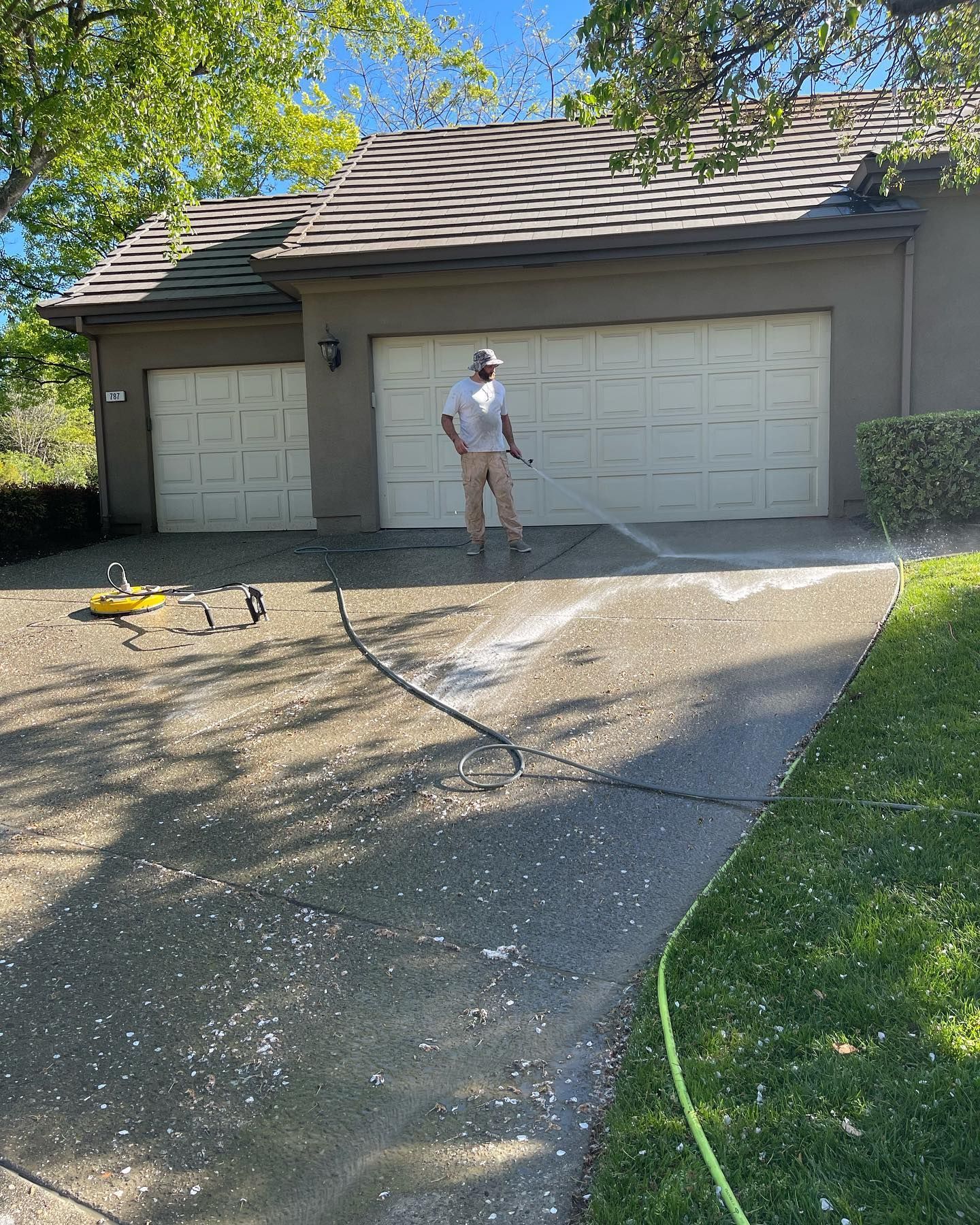 A man is standing in front of a garage with a hose.
