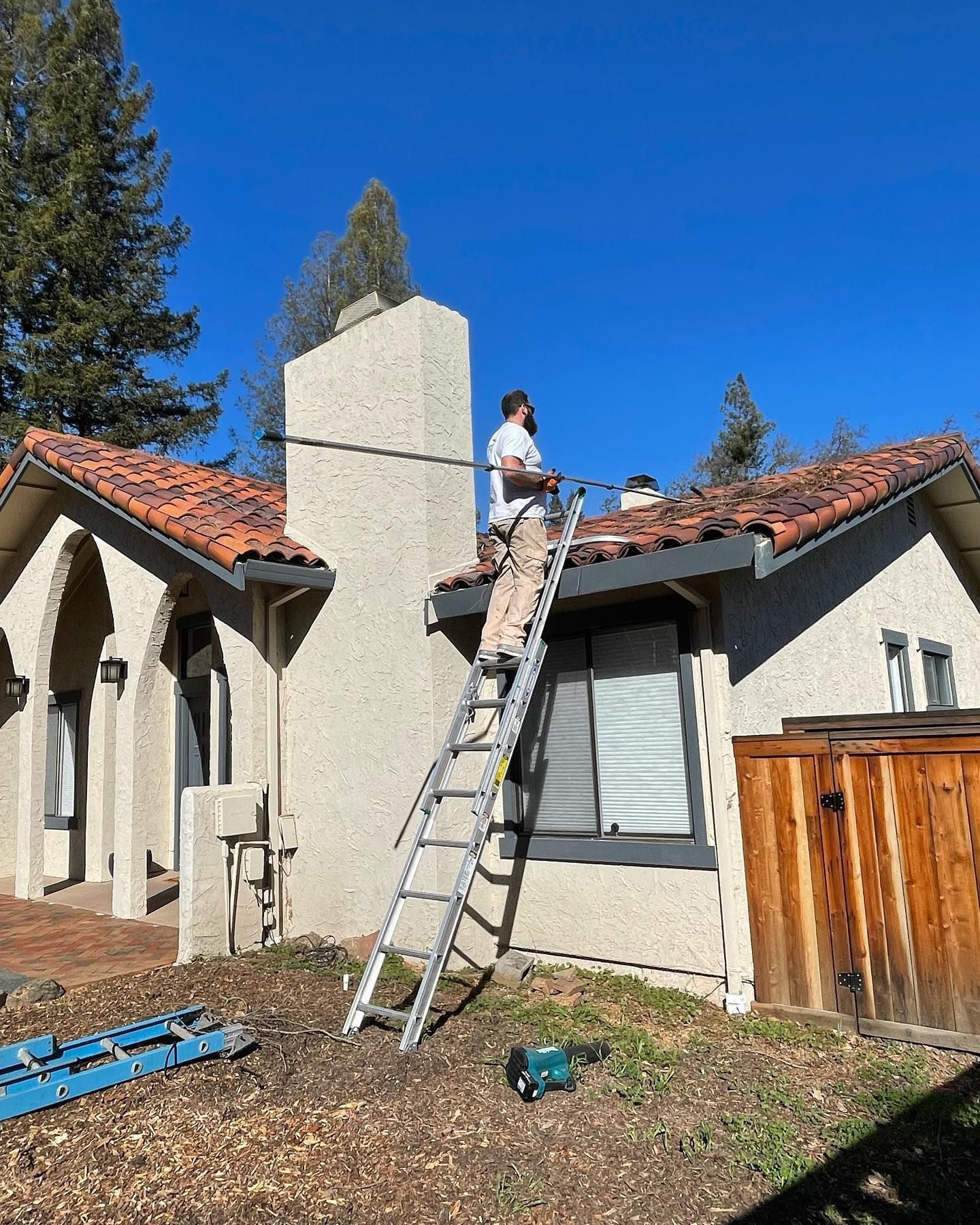 A man is standing on a ladder on the roof of a house.