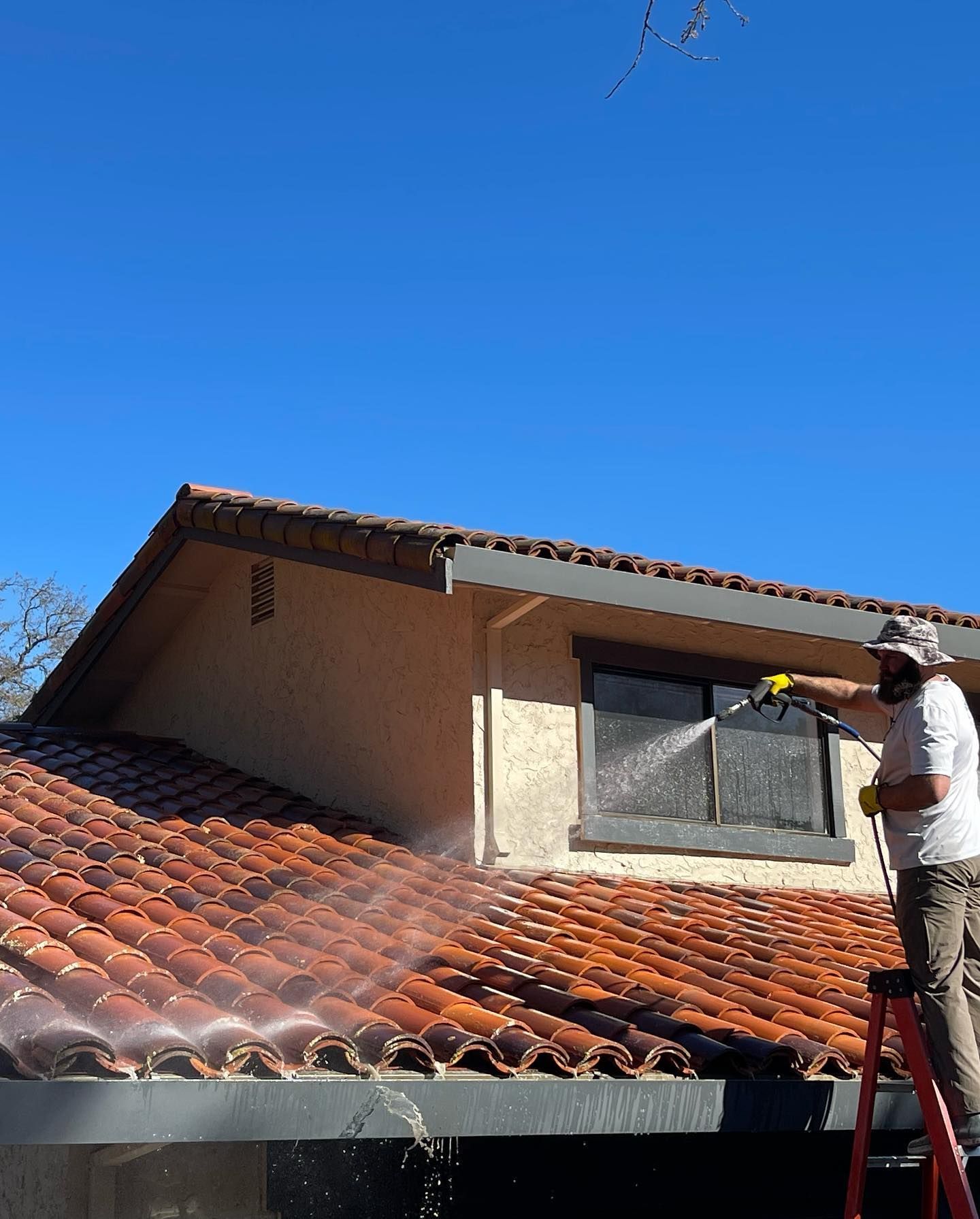A man is spraying water on the roof of a house.