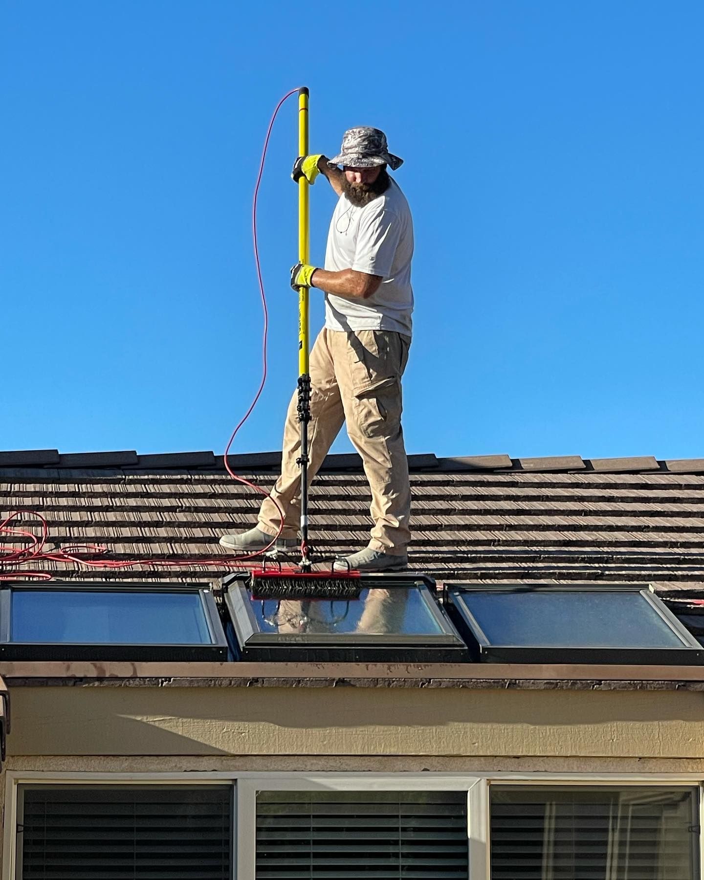 A man is standing on top of a roof holding a yellow pole.