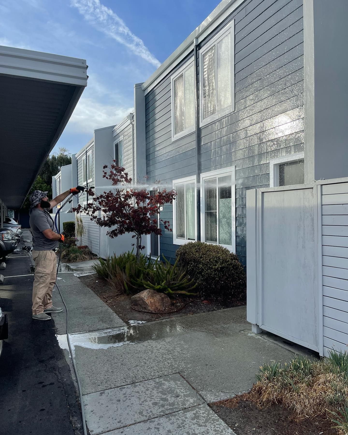 A man is cleaning the sidewalk in front of a building with a pressure washer.