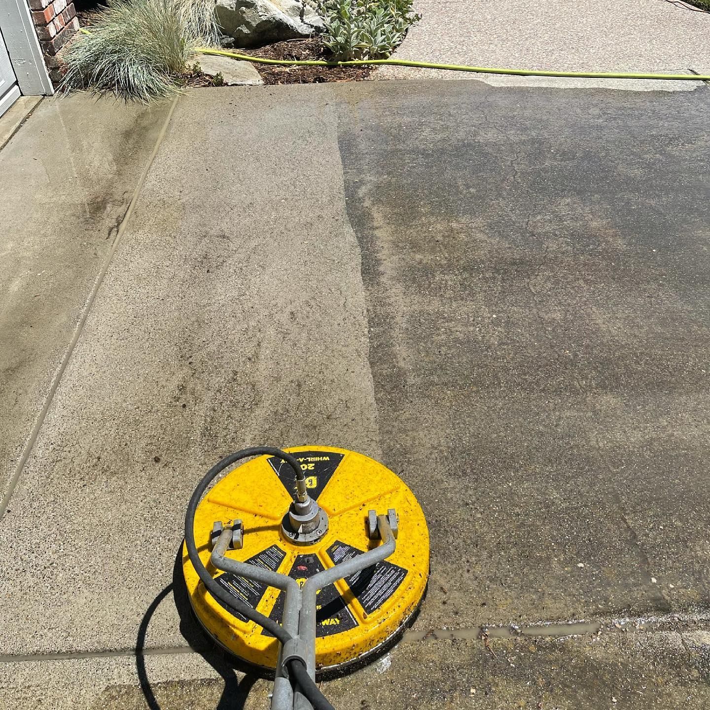 A yellow machine is being used to clean a concrete driveway.