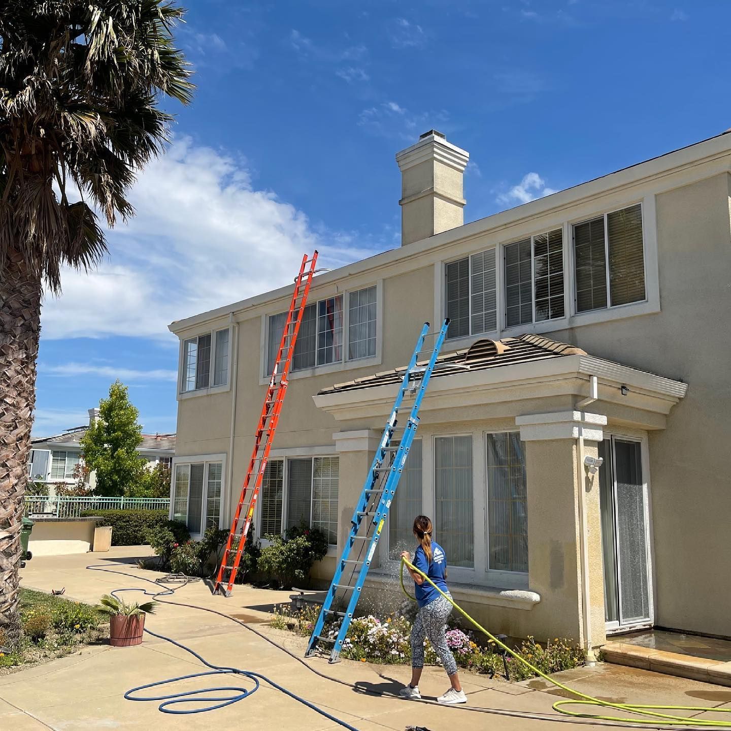 A woman is cleaning the windows of a house with a hose